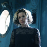 Singer Kate Rusby (who has blonde curly hair and wears a black lacy dress, against a blue background